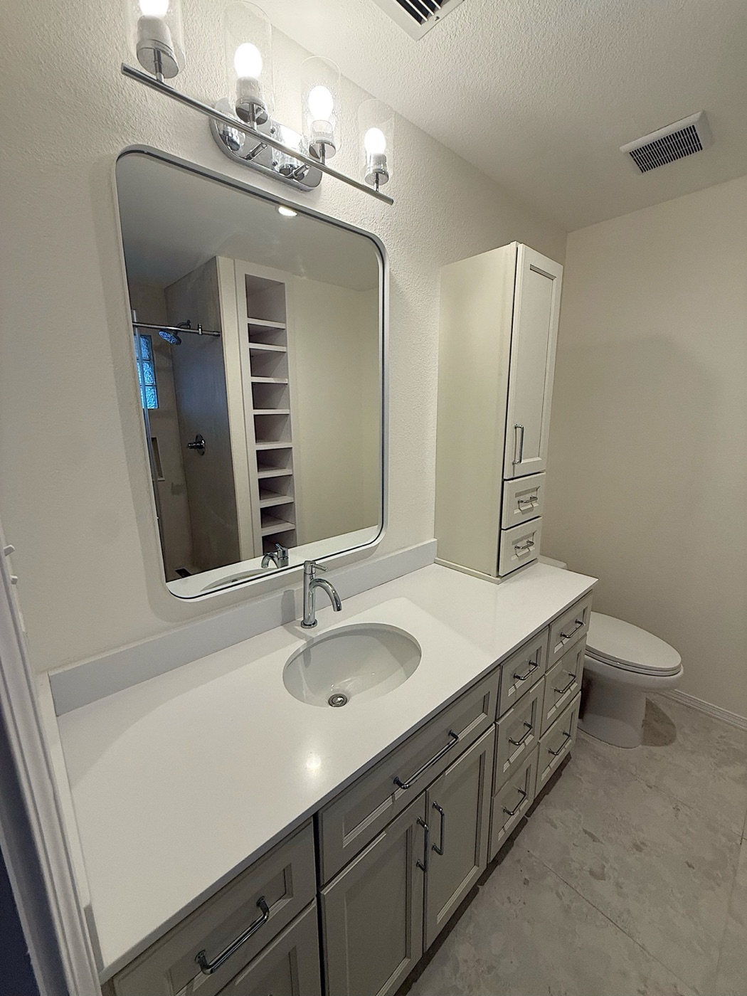 Finished bathroom with fresh paint, a shaker vanity, rounded mirror and four-light fixture