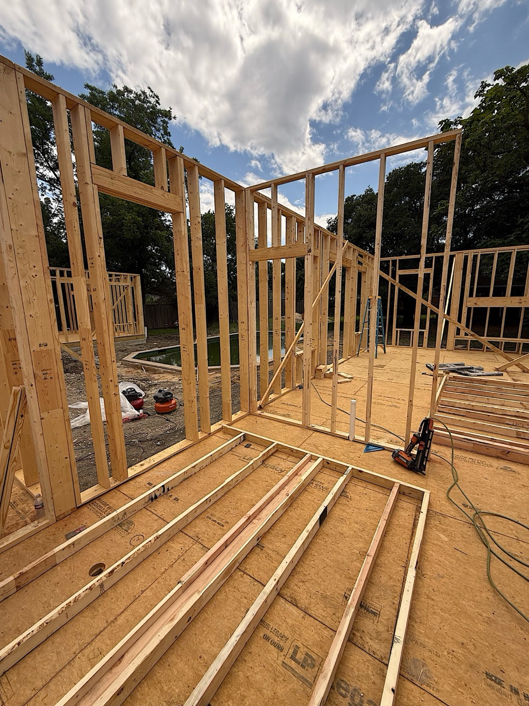 New wood-framed walls with door and window openings on an OSB subfloor under a blue sky