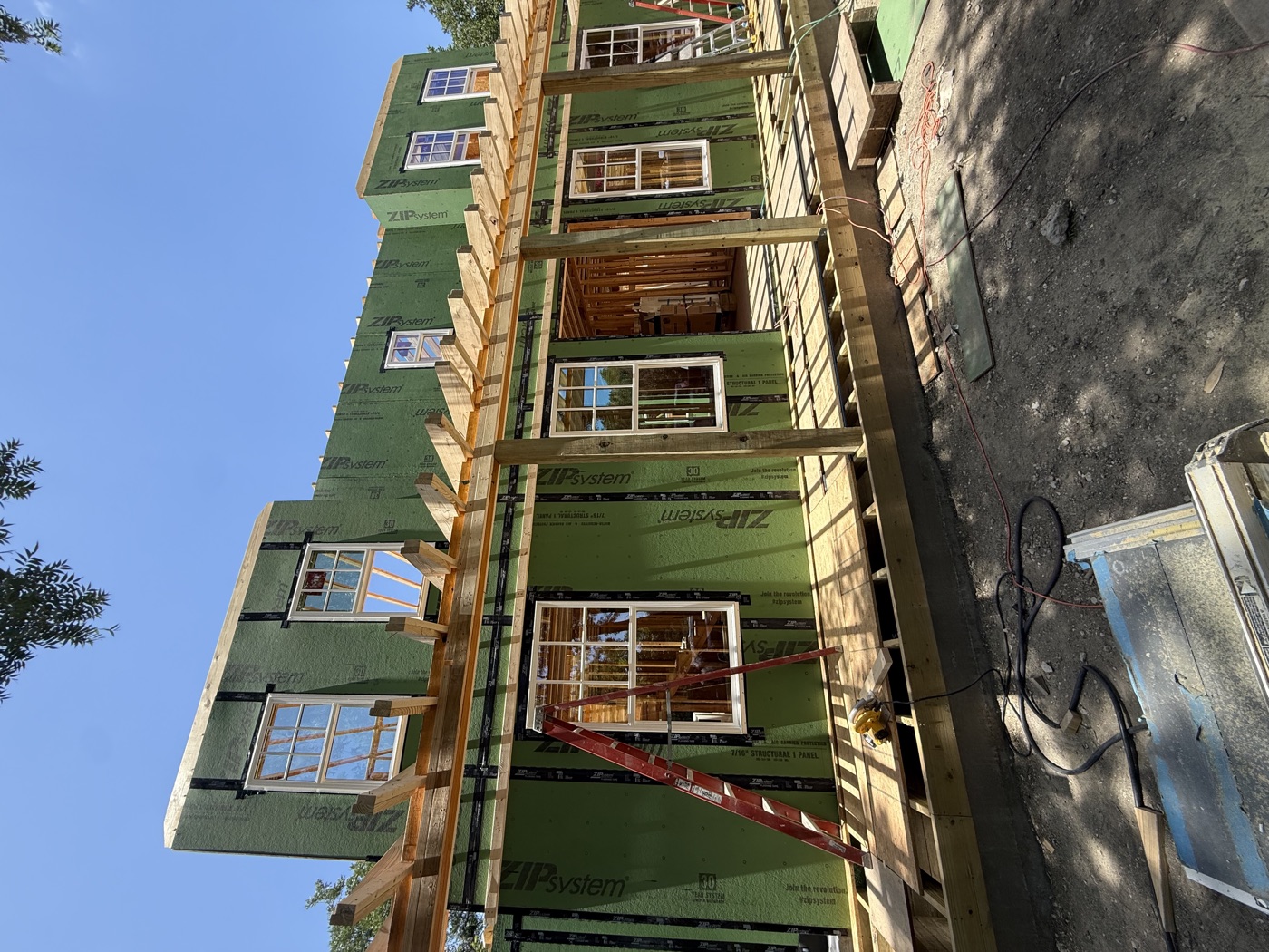 New house wrapped in green ZIP System sheathing with windows installed, porch deck and pergola framing across the front