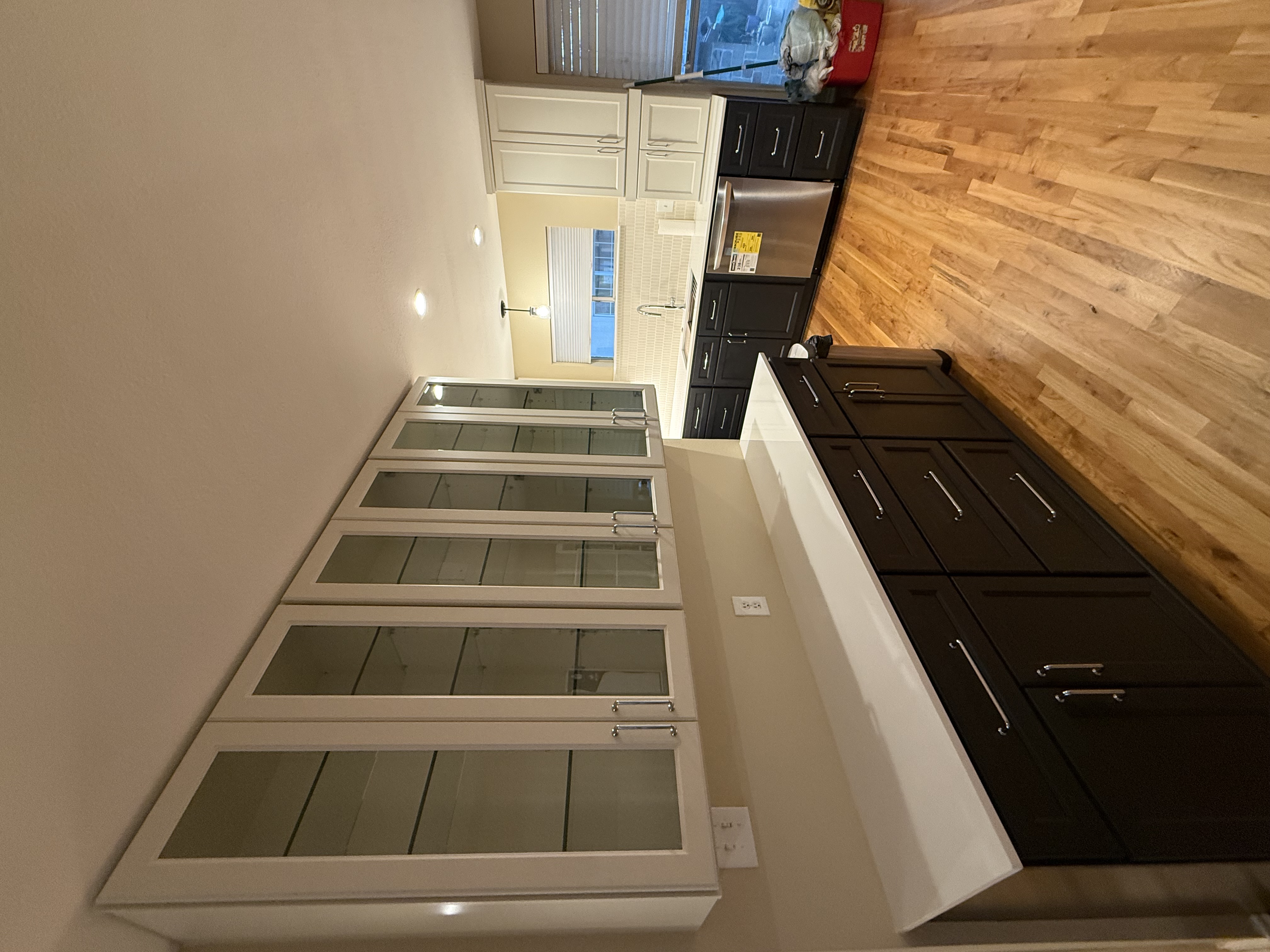 Kitchen with glass-front white upper cabinets, dark shaker base cabinets, white quartz counters, stainless dishwasher and oak floors