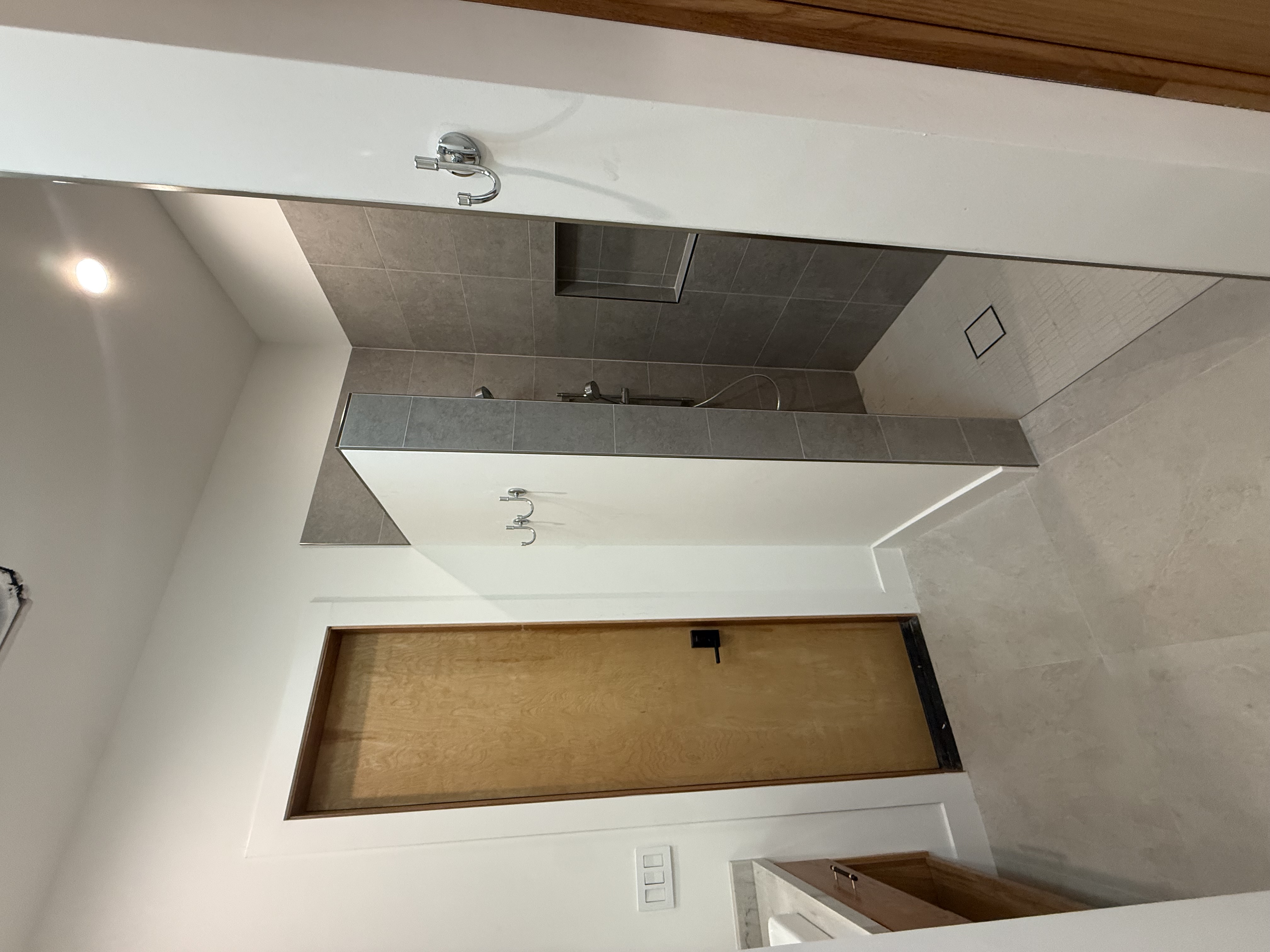 Bathroom with a curbless walk-in shower in gray tile with a recessed niche, large-format floor tile and a wood door