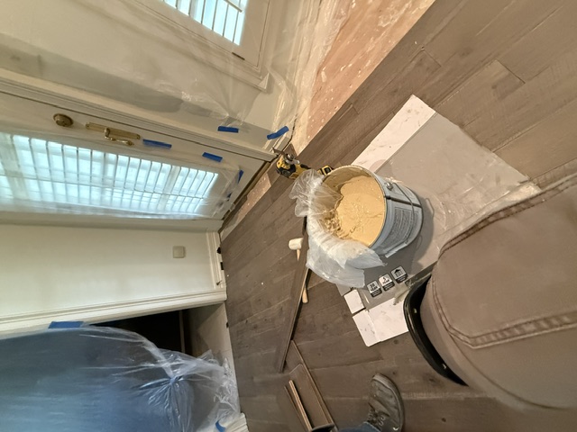 Room masked off with plastic sheeting and painter's tape, with an open can of paint and a roller on a protected floor
