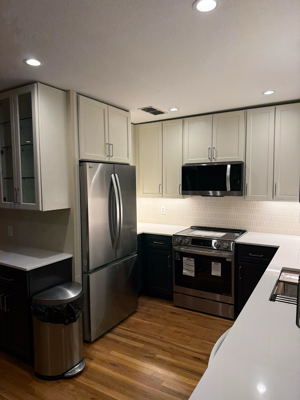 Remodeled kitchen with white upper cabinets, dark lower cabinets, white quartz counters and a stacked tile backsplash